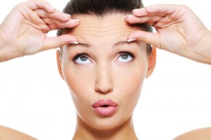 Woman with hands on forehead looking up at her wrinkles on her forehead